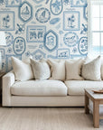 Ocean inspired toile wallpaper styled in a living room, adding timeless coastal charm with framed nautical illustrations and tropical motifs.