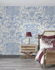 Blue and cream Dusky Garden Waltz damask wallpaper displayed on bedroom accent wall with ornate scrollwork pattern
