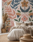 A gentle folk-art style wall covering depicting stylized berries, leaves, and blooms, rendered in warm ochre, dusty blue, muted pink, and sage green tones, set against a faint blush backdrop