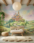 Whimsical fairy tale castle mural wallpaper in pastel watercolors on nursery accent wall with rattan crib