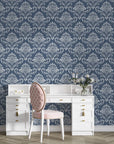Navy and silver damask wallpaper with ornate baroque motifs behind white vintage desk and pink chair