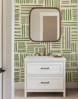 Hand-drawn blocks of olive green paint are laid out in an open, geometric grid structure on an abstract wall design with a warm, off-white background.