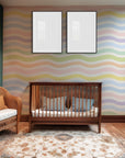 Horizontal, wavy stripes in muted pastel tones form a gentle rainbow pattern on this white wallpaper.