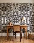 Aztec Quilt Espresso geometric tribal wallpaper behind a vintage writing desk in a cozy craft-room home office