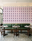 Ember & Iron Plum retro ogee wallpaper above a green leather banquette in a sunlit neighborhood cafe