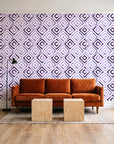 Fern Lattice Plum hand-drawn diamond wallpaper behind a rust velvet sofa in a bright coworking lounge