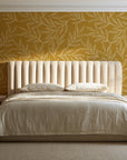 Forest Leaf Ochre botanical leaf wallpaper behind a channel-tufted bed in a calm primary bedroom