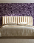 Grain Shift Aubergine minimalist dash wallpaper behind a channel-tufted bed in a calm primary bedroom