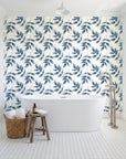 Harvest Crown Slate leafy branch wallpaper behind a freestanding tub in a bright coastal bathroom