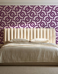 Indigo Labyrinth Plum geometric wallpaper behind a channel-tufted bed in a calm primary bedroom