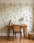 Ink & Sprig Bronze botanical sprig wallpaper behind a vintage writing desk in a cozy craft-room home office