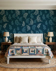 Ink & Sprig Peacock botanical sprig wallpaper behind a white cottage bed with a patchwork quilt in a cozy cottagecore bedroom