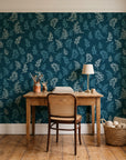 Ink & Sprig Peacock botanical sprig wallpaper behind a vintage writing desk in a cozy craft-room home office