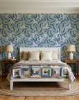 Magnolia Morning Slate magnolia bloom wallpaper behind a white cottage bed with a patchwork quilt in a cozy cottagecore bedroom