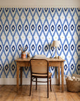 Ogee Loom Indigo ikat ogee wallpaper behind a vintage writing desk in a cozy craft-room home office