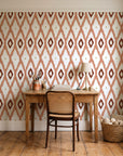 Ogee Loom Terracotta ikat ogee wallpaper behind a vintage writing desk in a cozy craft-room home office
