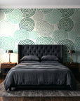 Petal Cascade Emerald spiral rosette wallpaper behind a tufted headboard in a dark, moody bedroom