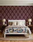 Rosewater Retreat Oxblood damask wallpaper behind a white cottage bed with a patchwork quilt in a cozy cottagecore bedroom