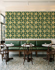 Solar Ritual Emerald floral wallpaper above a green leather banquette in a sunlit neighborhood cafe