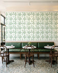Solar Ritual Sage floral wallpaper above a green leather banquette in a sunlit neighborhood cafe