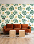 Solstice Bloom Emerald folk sun wallpaper behind a rust velvet sofa in a bright coworking lounge
