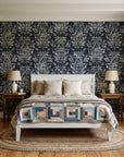 Tranquil Flora Onyx floral damask wallpaper behind a white cottage bed with a patchwork quilt in a cozy cottagecore bedroom