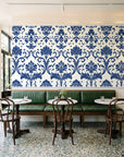 Twilight Garden Veil Indigo damask wallpaper above a green leather banquette in a sunlit neighborhood cafe