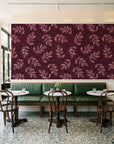 Verdant Scatter Oxblood tossed leaf wallpaper above a green leather banquette in a sunlit neighborhood cafe