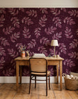 Verdant Scatter Oxblood tossed leaf wallpaper behind a vintage writing desk in a cozy craft-room home office
