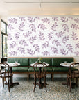 Verdant Scatter Plum tossed leaf wallpaper above a green leather banquette in a sunlit neighborhood cafe