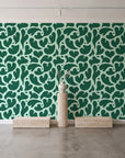 Woven Whisper Emerald abstract heart wallpaper behind a travertine pedestal and vase in a minimal boutique