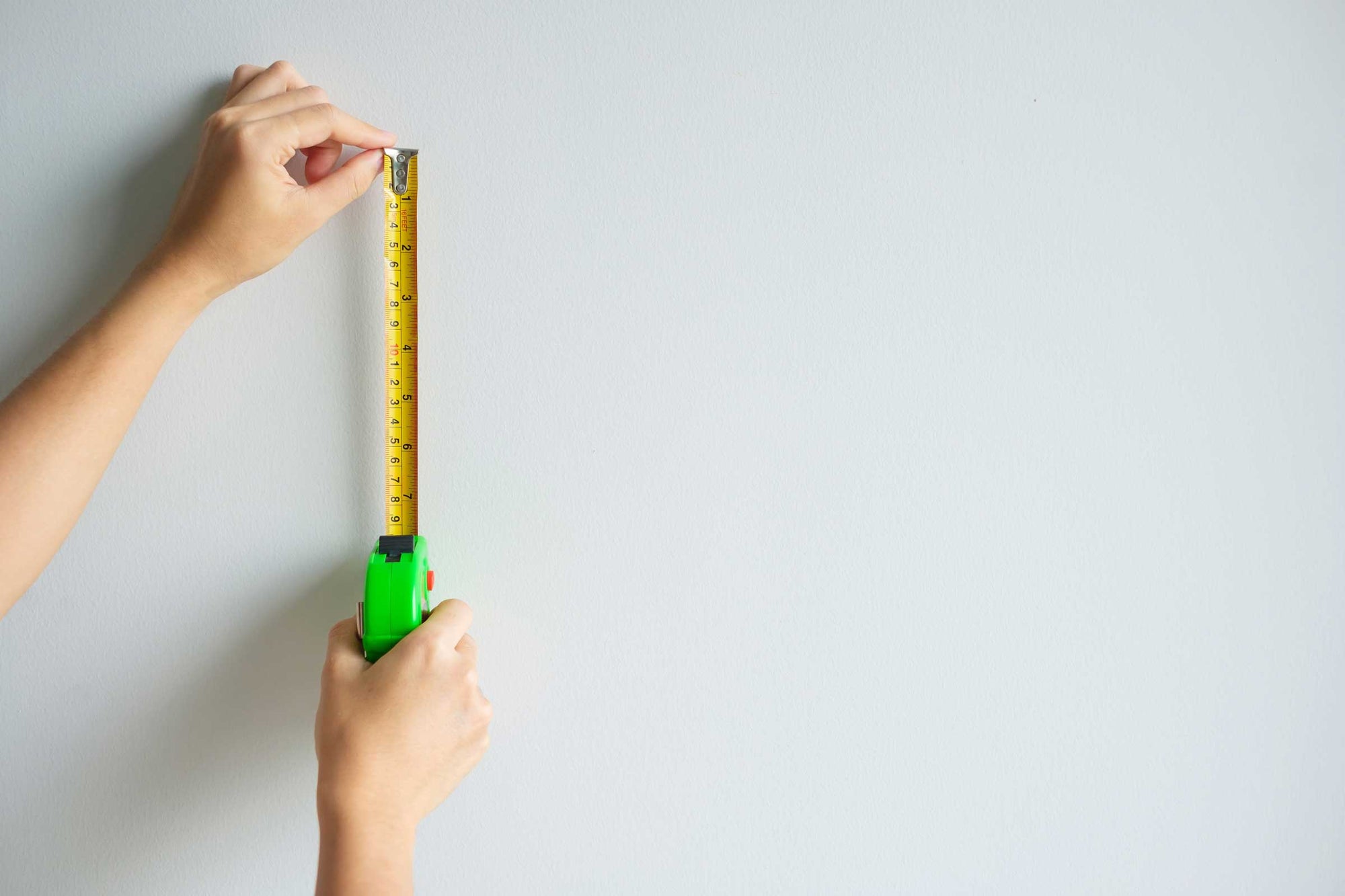 Person measuring a wall with a steel tape measure for custom wallpaper ordering