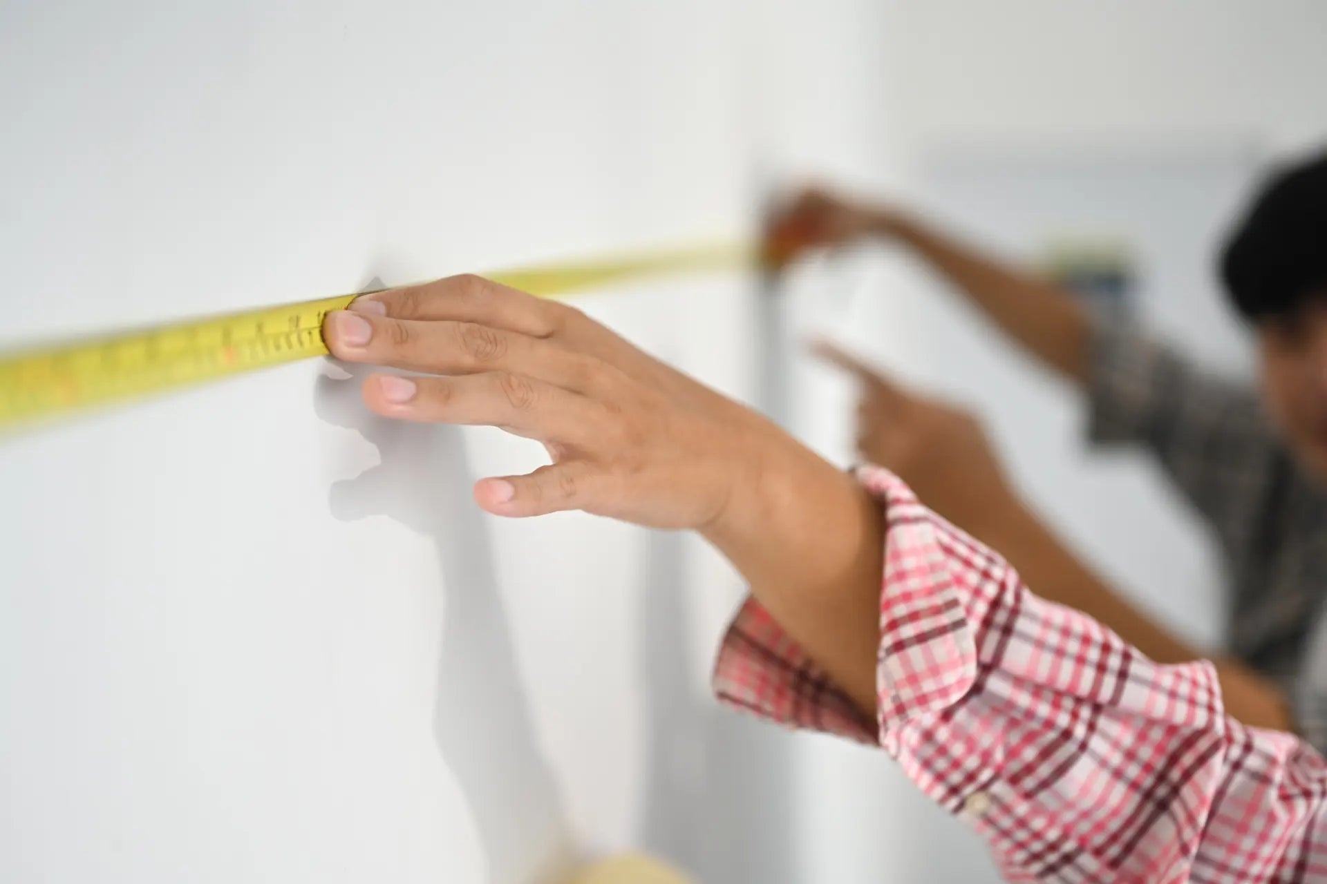 Hand holding tape measure across wall to measure wallpaper