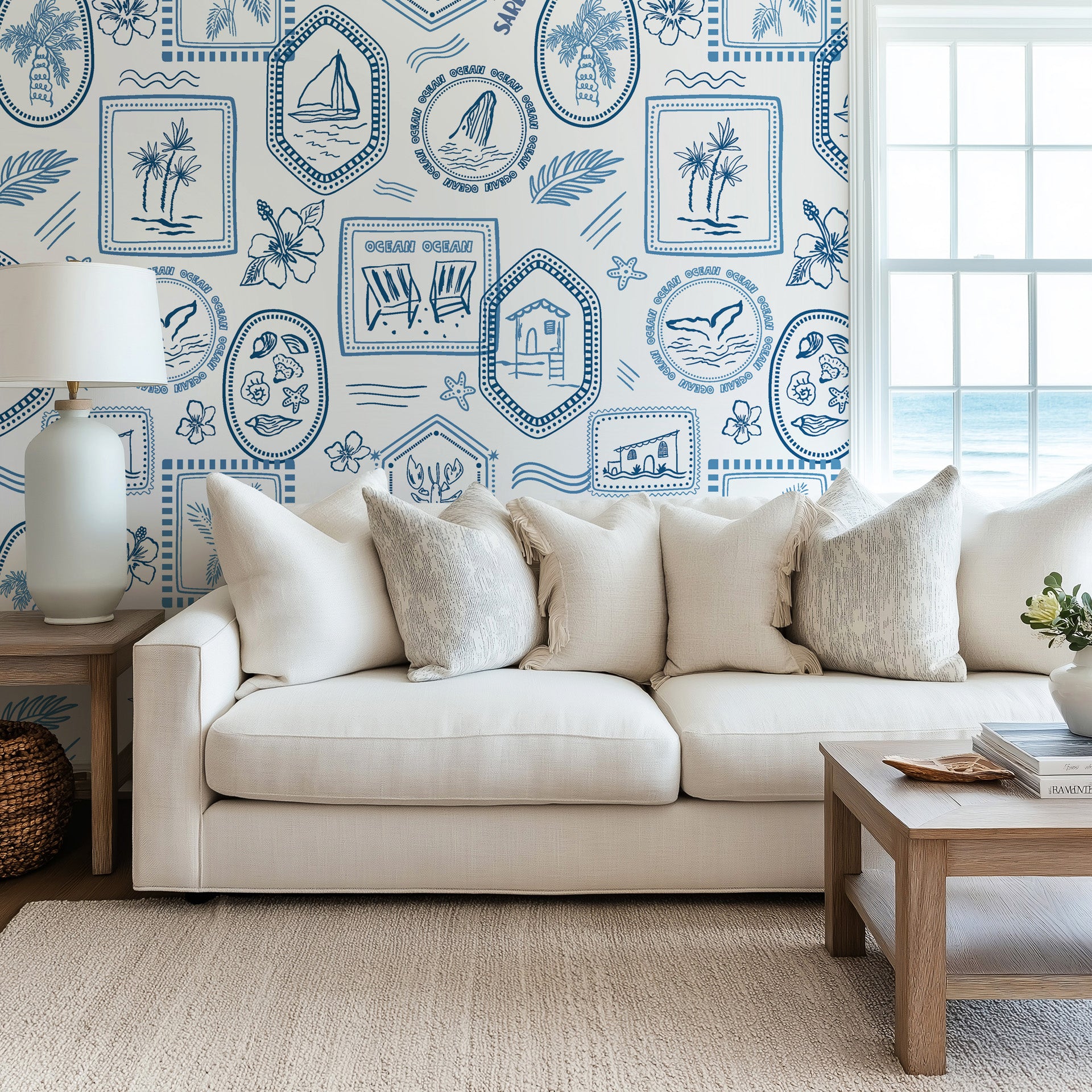 Ocean inspired toile wallpaper styled in a living room, adding timeless coastal charm with framed nautical illustrations and tropical motifs.