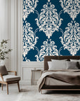 Classic damask wallpaper with crisp ivory ornamental scrollwork on a deep teal blue background.
