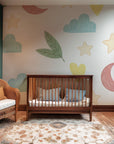 Whimsical nursery wallpaper with pastel moons, stars, clouds, leaves, and hearts scattered across a soft white background.