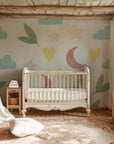 Whimsical nursery wallpaper with pastel moons, stars, clouds, leaves, and hearts scattered across a soft white background.