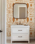 This iconographic Western wallpaper utilizes a warm palette of clay and earth tones to depict desert landscapes, snakes, moons, boots, and horseshoes.