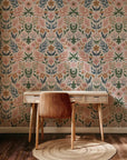 A soft botanical motif wallpaper in a stylized folk-art fashion. The design includes flowers, leaves, and berries, utilizing muted colors like sage green, warm ochre, dusty blue, and pale pink, all against a blush base.