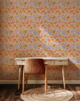 A botanical wallpaper featuring hand-painted abstract leaf and flower designs in peach, ochre, lavender, and soft coral, contrasted with a warm cream base color.