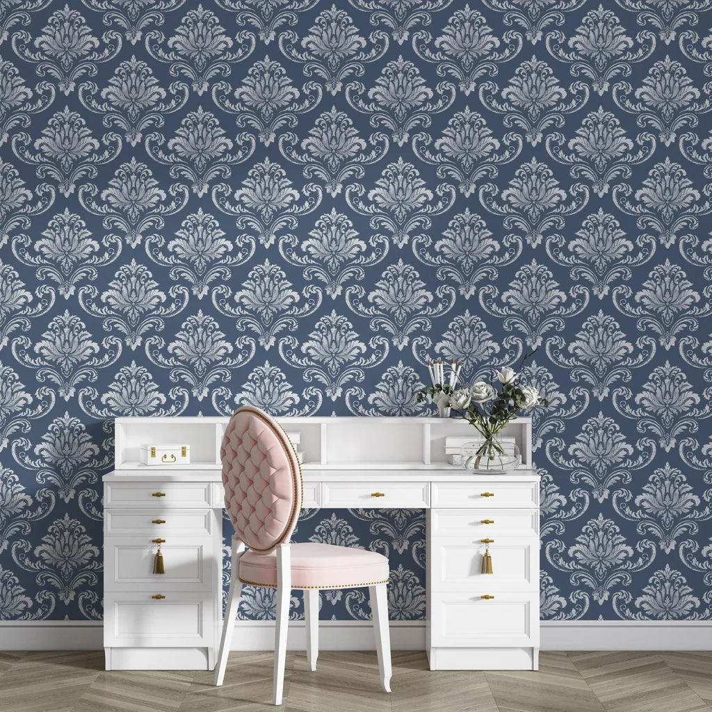 Navy and silver damask wallpaper with ornate baroque motifs behind white vintage desk and pink chair