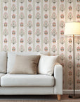 Vertical floral stripe wallpaper with symmetrical folk inspired flowers in red, olive green, and soft peach on a warm cream background.