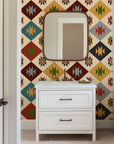 Southwestern geometric wallpaper with repeating diamond motifs in warm earth tones including rust red, mustard yellow, sage green, teal, charcoal, and ivory.