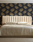 Acacia Scatter Black Gold dainty leaf wallpaper behind a channel-tufted bed in a calm primary bedroom