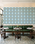 Andalusian Court Peacock encaustic tile wallpaper above a green leather banquette in a sunlit neighborhood cafe