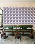 Andalusian Court Plum encaustic tile wallpaper above a green leather banquette in a sunlit neighborhood cafe
