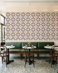 Andalusian Court Terracotta encaustic tile wallpaper above a green leather banquette in a sunlit neighborhood cafe