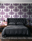 Antique Fern Mist Aubergine distressed damask wallpaper behind a tufted headboard in a dark, moody bedroom