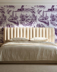 Arcadian Reverie Plum pastoral toile wallpaper behind a channel-tufted bed in a calm primary bedroom