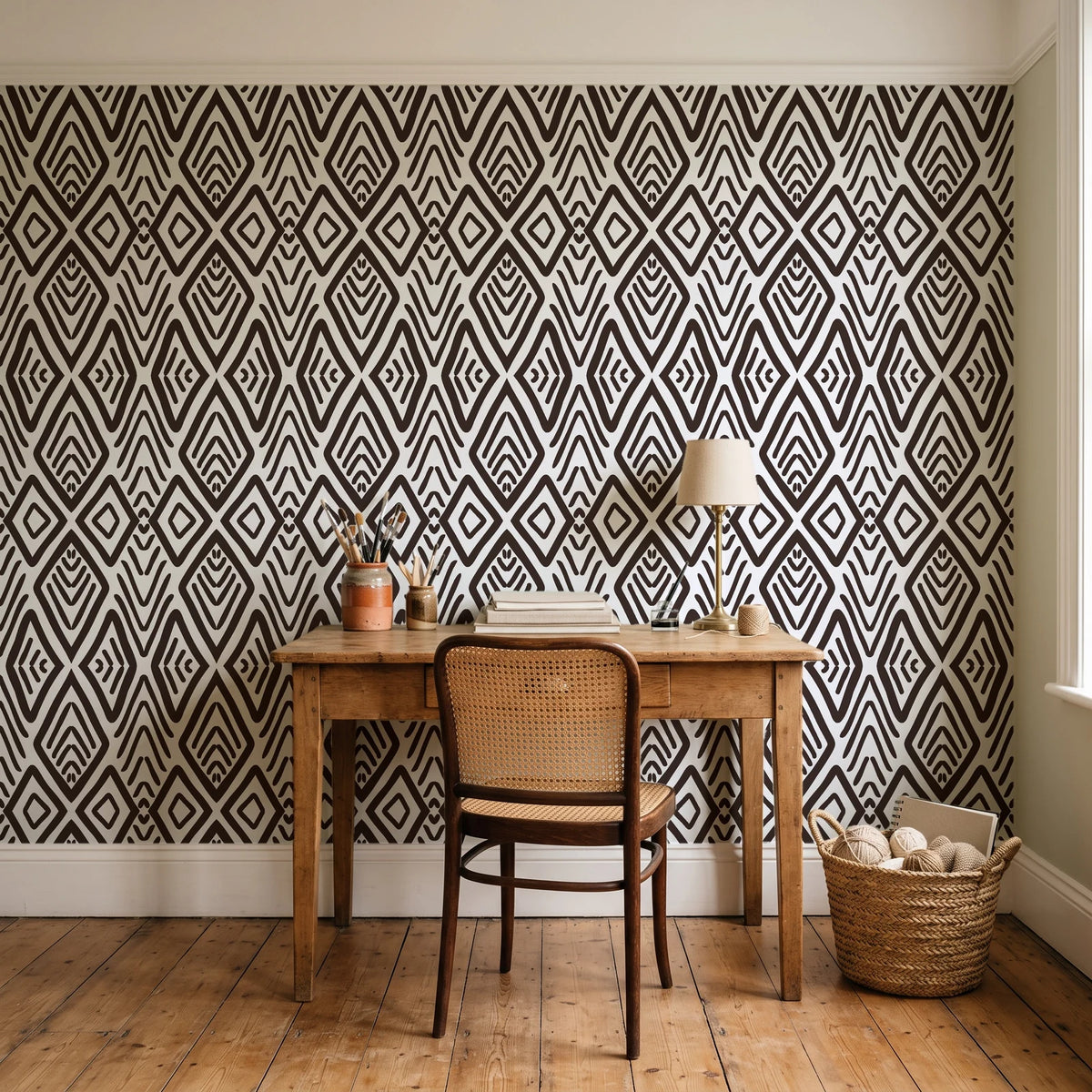 Aztec Quilt Espresso geometric tribal wallpaper behind a vintage writing desk in a cozy craft-room home office